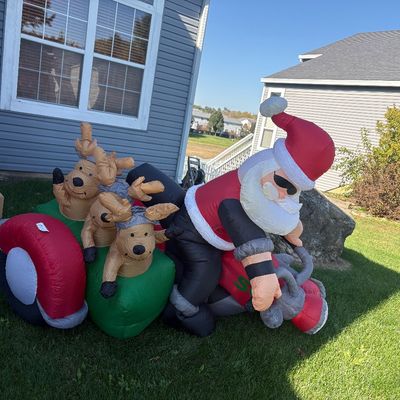 Large outdoor Christmas inflatable featuring Santa Claus riding a motorcycle with reindeer in a sidecar.