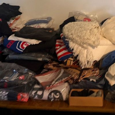 Sale Photo Thumbnail #42: Large assortment of folded clothing, graphic t-shirts, sweaters, blankets, and textiles stacked on a wooden table.