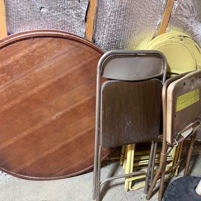 Sale Photo Thumbnail #102: Round wooden table top stored alongside several metal and wood-grain folding chairs, showing light surface wear.