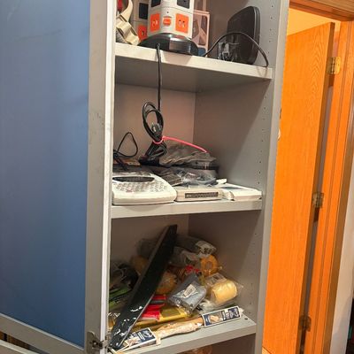 Sale Photo Thumbnail #79: Tall grey and blue cabinet filled with assorted electronics, office supplies, and household hardware.