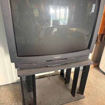 Sale Photo Thumbnail #97: Vintage Magnavox CRT television sitting on a black media stand with built-in media storage slots.