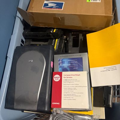 Sale Photo Thumbnail #34: Plastic laundry basket filled with vintage electronics, including an HP flatbed scanner, Compaq software documentation, server drive caddies, and cables.