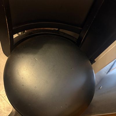 Sale Photo Thumbnail #4: Black wooden swivel bar stool featuring a padded faux leather round seat and backrest, showing light wear.