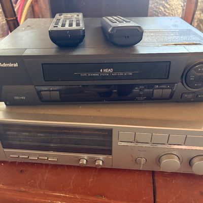 Sale Photo Thumbnail #92: Black Admiral 4-head VHS VCR player with two remote controls stacked on top of a vintage Proformance silver stereo receiver.
