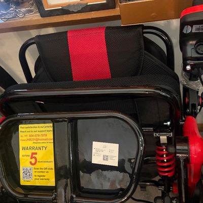 Sale Photo Thumbnail #26: Foldable electric power wheelchair featuring a black and red frame, mesh upholstery, rear suspension springs, and a joystick controller unit.