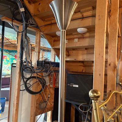 Sale Photo Thumbnail #120: Contemporary brushed metal torchiere floor lamp with a flared trumpet-style shade, shown in an unfinished basement area.