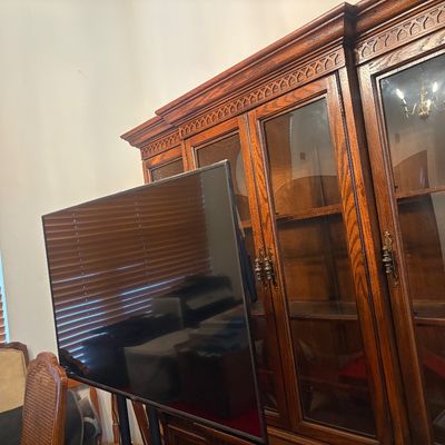 Sale Photo Thumbnail #19: Large wooden hutch with glass cabinet doors and decorative carved trim, shown behind a flat-screen television.