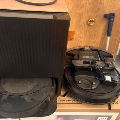 Sale Photo Thumbnail #18: Black robot vacuum unit seated in its self-emptying base station alongside a second robot vacuum body and charging dock, showing light wear and dust.