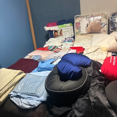 Sale Photo Thumbnail #83: Assortment of modern household linens, including bed sheets, comforters in original packaging, travel pillows, and folded blankets laid out on a bed.