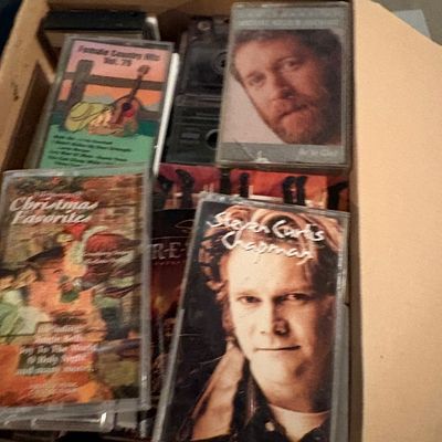 Sale Photo Thumbnail #121: Cardboard box filled with assorted cassette tapes, including titles by Steven Curtis Chapman and Michael Kelly Blanchard.
