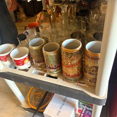 Sale Photo Thumbnail #80: Collection of vintage glassware and beer steins, including Stroh's beer steins and Campbell's Soup mugs, displayed on a plastic utility shelf.