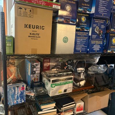 Sale Photo Thumbnail #6: Black metal shelving unit loaded with various boxed items, including a Keurig K-Elite coffee maker, Franklin Mint die-cast motorcycle collectibles, lighting fixtures, sports memorabilia, and books.