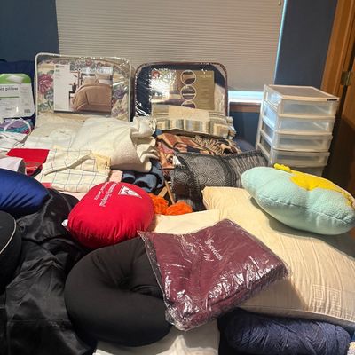 Sale Photo Thumbnail #82: Large assortment of bedding items, including packaged comforter sets, throw pillows, neck travel pillows, blankets, and folded linens, alongside a small plastic drawer organizer.