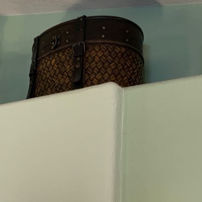 Sale Photo Thumbnail #115: Woven basket-style chest with leather straps and metal hardware, stored atop a high ledge.