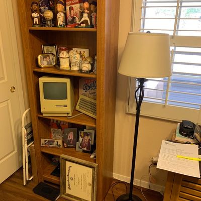 Sale Photo Thumbnail #88: Tall oak bookshelf filled with sports memorabilia, framed photos, and a vintage Macintosh computer, alongside a wrought iron floor lamp.