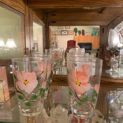 Sale Photo Thumbnail #54: Set of vintage clear glass tumblers featuring hand-painted pink floral motifs with green leaves, displayed in a wooden hutch.