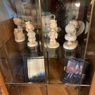 Sale Photo Thumbnail #43: Collection of Precious Moments porcelain figurines and framed photos displayed inside a glass-door curio cabinet.