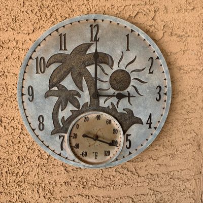 Sale Photo Thumbnail #31: Round tropical-themed outdoor wall clock with built-in thermometer, featuring raised palm tree and sun relief detail on a stone-look finish.