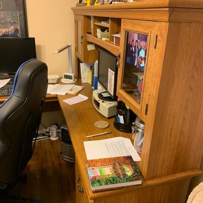 Sale Photo Thumbnail #90: Large wooden L-shaped home office desk with matching upper hutch featuring glass-front cabinets and open cubbies.
