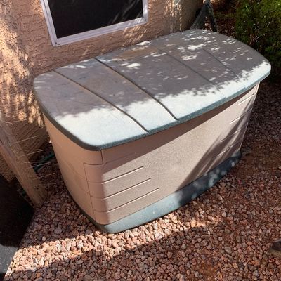 Sale Photo Thumbnail #25: Large outdoor resin deck box in beige and green, sitting on a gravel bed next to a house wall.