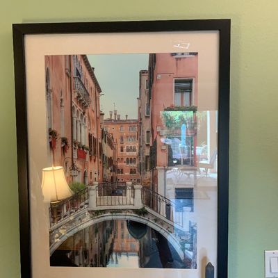 Sale Photo Thumbnail #35: Framed photographic print depicting a scenic Venetian canal with a stone bridge and historic architecture, presented in a black frame with a white mat.