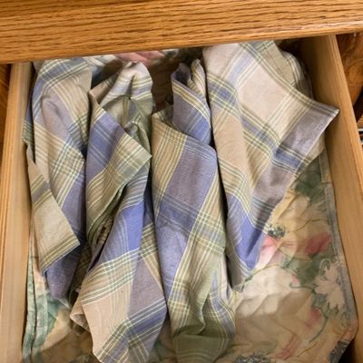 Sale Photo Thumbnail #58: Open wooden furniture drawer filled with folded plaid and floral pattern linens.