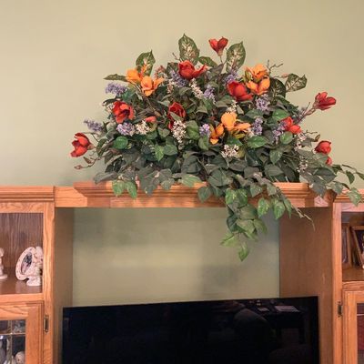 Sale Photo Thumbnail #39: Large faux floral and greenery arrangement featuring orange and red blossoms, displayed atop a traditional light oak entertainment center.