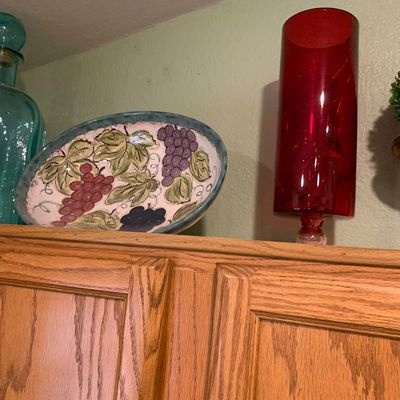 Sale Photo Thumbnail #72: Hand-painted Tuscan-style ceramic grape motif platter alongside a tall red glass cylinder vase displayed atop oak cabinetry.
