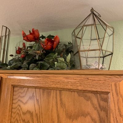 Sale Photo Thumbnail #76: Geometric brass and glass terrarium lantern filled with fairy lights, displayed alongside artificial red flowers atop a wooden cabinet.