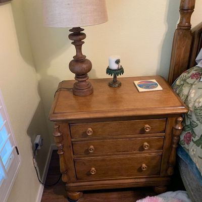 Sale Photo Thumbnail #93: Traditional wooden three-drawer nightstand topped with a turned wood table lamp featuring a beige shade.