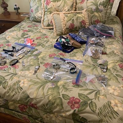 Sale Photo Thumbnail #102: Assortment of women's watches, jewelry in clear plastic bags, and small fabric pouches laid out on a tropical floral print comforter.
