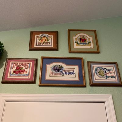 Sale Photo Thumbnail #70: Set of five framed needlepoint cross-stitch artworks featuring vintage fruit crate label designs, including peaches, cherries, plums, blueberries, and pears.