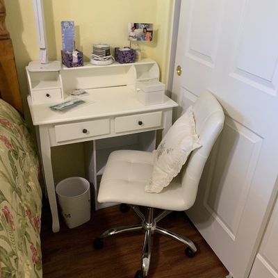 Sale Photo Thumbnail #101: White wooden writing desk with small storage drawers and raised hutch, paired with a modern white faux leather rolling desk chair.