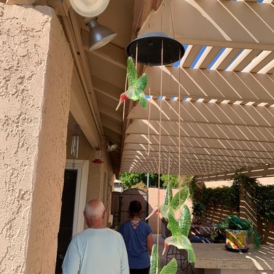 Sale Photo Thumbnail #28: Hanging solar-powered mobile featuring green glass hummingbird figures, suspended under a patio pergola.