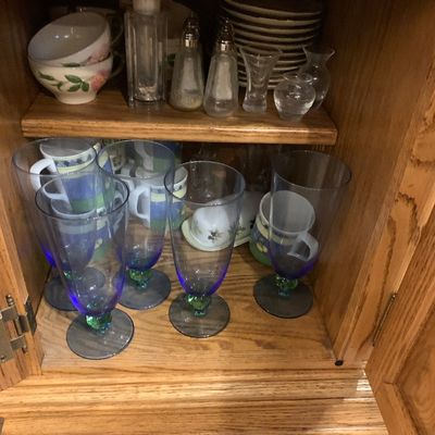 Sale Photo Thumbnail #56: Oak cabinet filled with glassware, including blue and green stemmed glasses, tea cups, salt and pepper shakers, and stacked plates.