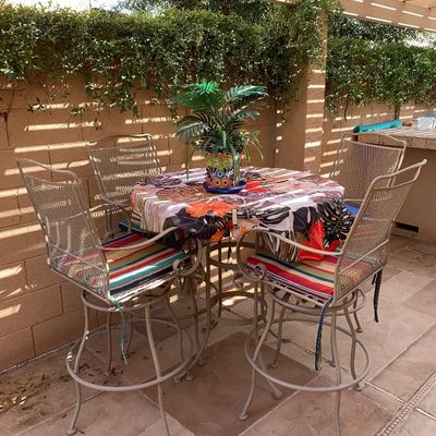 Sale Photo Thumbnail #3: Five-piece outdoor patio dining set, including a round high-top table and four wrought iron swivel barstools with colorful seat cushions.