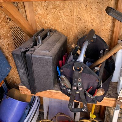 Sale Photo Thumbnail #18: Black hard plastic tool case resting on a wooden workbench next to a soft-sided tool tote bag filled with hand tools.