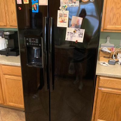 Sale Photo Thumbnail #64: Black GE side-by-side refrigerator featuring an exterior ice and water dispenser, displayed between oak kitchen cabinets.