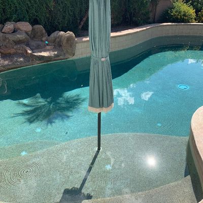 Sale Photo Thumbnail #10: Folded light teal outdoor patio umbrella with fringe trim, positioned in an in-pool Baja shelf socket.