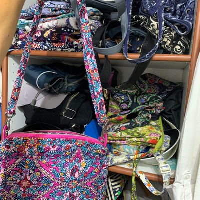 Sale Photo Thumbnail #113: Vera Bradley colorful floral quilted crossbody bag held in front of a closet shelf stacked with additional quilted handbags and purses.