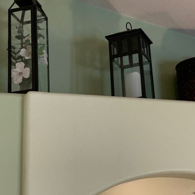 Sale Photo Thumbnail #116: Two modern black metal and glass decorative lanterns displayed on a ledge, one containing faux flowers and the other with a white pillar candle.
