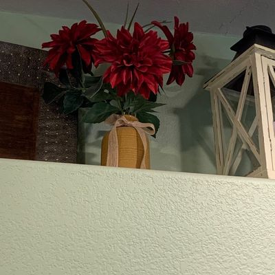 Sale Photo Thumbnail #79: Faux red dahlia arrangement in a yellow ribbed ceramic vase tied with a fabric bow, displayed alongside a white decorative lantern.
