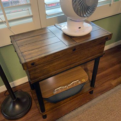 Sale Photo Thumbnail #109: Rustic modern wooden side table featuring a lift-top storage compartment, black metal legs, and a lower shelf, shown with a white Woozoo globe fan resting on top.