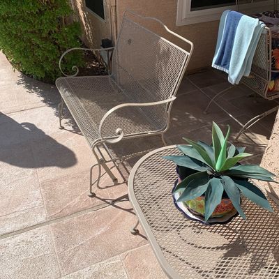 Sale Photo Thumbnail #13: Vintage beige expanded metal patio set featuring a scroll-arm glider bench and a matching oval coffee table holding a potted artificial agave plant.