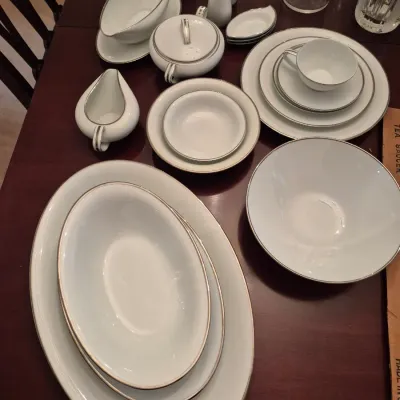 Sale Photo Thumbnail #68: Collection of white fine china dishware with silver trim, including serving platters, a gravy boat, salt and pepper shakers, and place settings.