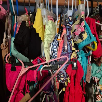 Sale Photo Thumbnail #67: Collection of women's swimsuits and bikini tops in various colors and patterns, hanging together in a closet.