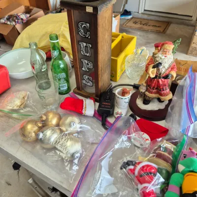 Sale Photo Thumbnail #38: Collection of assorted estate items including a vintage wooden cup dispenser, Santa Claus figurine, Christmas ornaments, glass bottles, and holiday decorations.