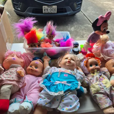 Collection of vintage baby dolls, troll dolls with colorful hair, and a Minnie Mouse figure arranged on a folding table at a garage sale.