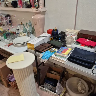 Sale Photo Thumbnail #12: White fluted pedestal stand alongside folding tables displays various household items, glassware, books, and small electronics.