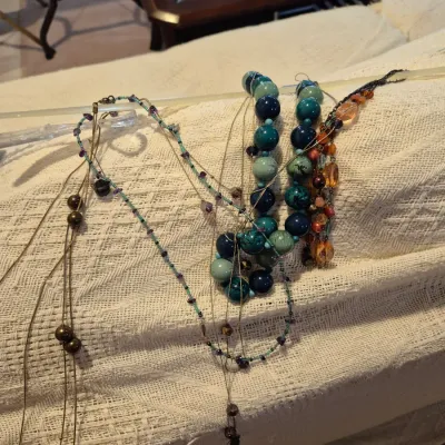 Sale Photo Thumbnail #65: Collection of fashion necklaces featuring teal chunky beaded strands, delicate chain drops, and amber-toned beaded designs.